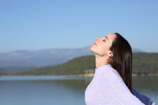 Side view portrait of a relaxed woman breathing fresh air in a mountain lake