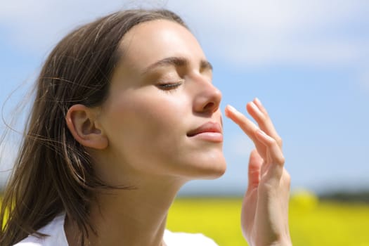 Portrait of a beautiful woman putting moisturizer cream on cheek in a field