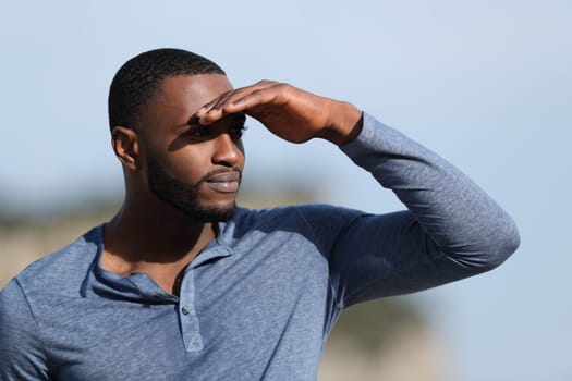 Serious man with black skin searching protecting from sun with a hand in the mountain a sunny day