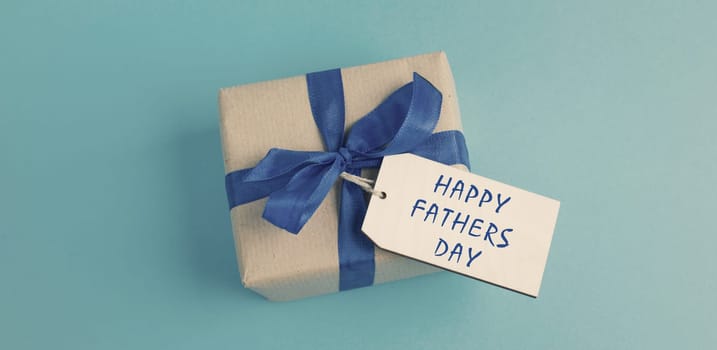 Small gift box with a ribbon on a blue colored background, happy fathers day present
