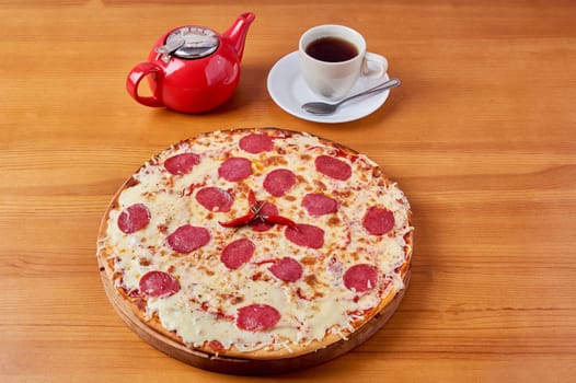 italian pepperoni pizza with red pepper on a wooden stand with tea and kettle. High quality photo