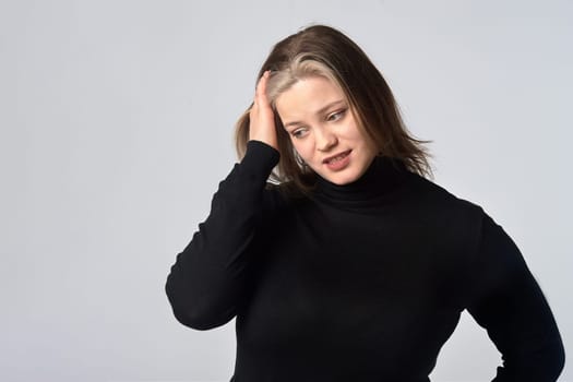 a distressed woman in a black sweater holds her head against a gray background. High quality photo