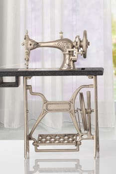 Beautiful miniature model of a vintage sewing machine on bright table over abstract bright curtain background. Advertisement for tailor business. Space for text and montage.