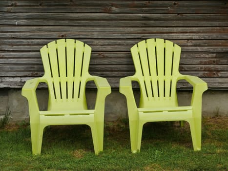 yellow plastic lounge chairs on the lawn by the wall of a country house in the backyard