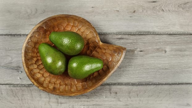Tabletop view, three avocado pears on wooden carved bowl