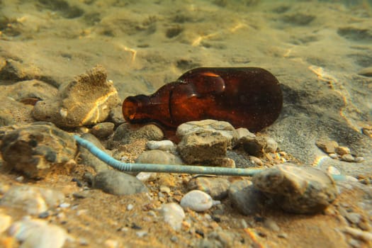 Beer bottle and plastic straw on sand sea bottom. Underwater photo, ocean littering / pollution concept.