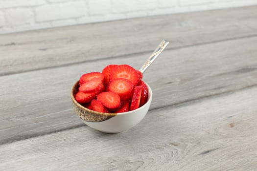 Small bowl full of strawberry pieces, spoon - healthy snack ready to eat.