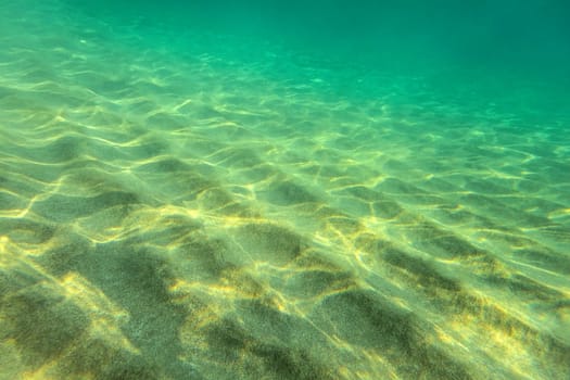 Sandy sea bottom, small sand "dunes"" lit by sun, underwater photo, abstract marine background."