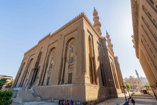 Cairo, Egypt - November 27 2021: Facade of Islamic Royal era Mosque of Al Rifai, with side view of Mamluk era Mosque and Madrassa of Sultan Hassan, with few visitors, Old Cairo