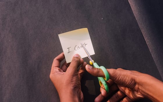 Hands cutting letter T from can’t with scissors written text on rectangle reminder paper. Determination Success Challenge believe Motivation aspirations to achieve results Aim goal Business concept.