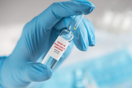 Coronavirus modified omicron vaccine in hand with blue protective gloves.