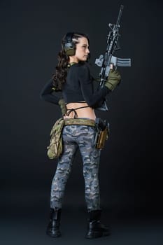 A young woman with a rifle stands with her back against a black background. High quality photo