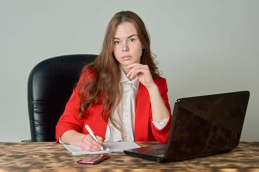 A woman sitting at a desk working with a laptop and notepad. High quality photo
