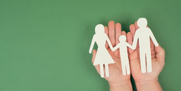 Parents with one child holding hands, paper cut out, copy space, petrol colored background, relationship family