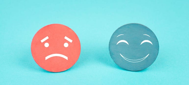 Two faces, smiling and sad in different colors on a blue background, copy space, rating, communication, customer feedback