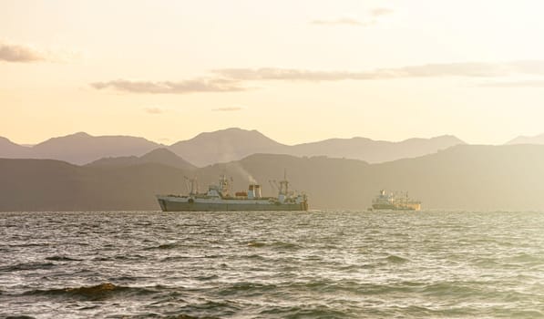 The fishing ship in the sea at sunrise on the background of mountains