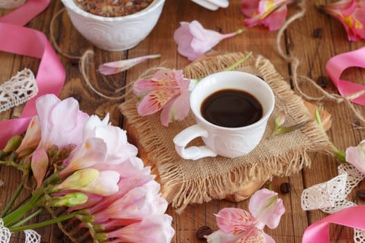 Coffee cup near flowers and ribbons close up on wooden table. Romantic Breakfast, valentines day concept