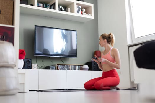 Attractive sporty woman working out at home, doing pilates exercise in front of television in small studio appartment. Social distancing. Stay healthy and stay at home during corona virus pandemic.