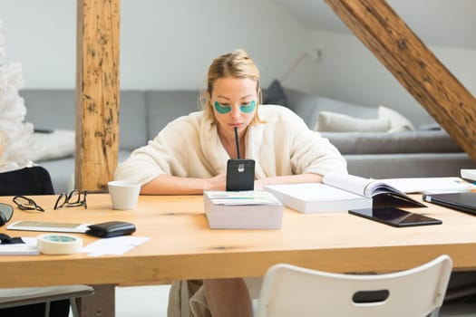 Young businesswoman wearing cosy warm bathrobe having remote cell phone conference call meeting from home living room in winter Christmas time. Remote work from home concept