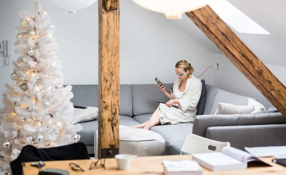 Young businesswoman wearing cosy warm bathrobe working remotly from home in winter Christmas time during 2020 corona virus pandemic. Work from home, selter in place, concept.