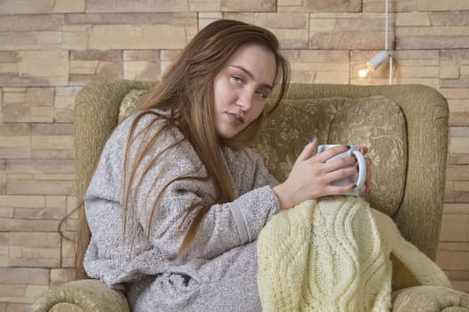 a girl in a chair with a cup of coffee covered with a blanket. High quality photo