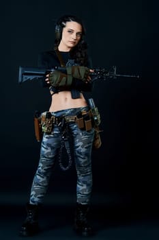 Dressed in a black T-shirt, a curvy combat woman with short hair holds a rifle against a dark background. High quality photo