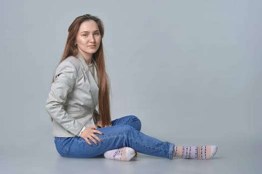Young woman sitting on gray background in studio. High quality photo
