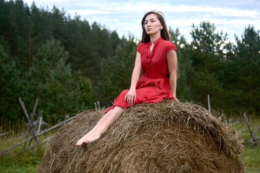 a girl in a red dress sits on a haystack and looks into the distance. High quality photo