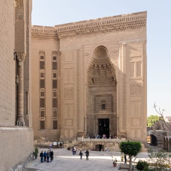 Cairo, Egypt - November 27 2021: Facade of Islamic Mamluk era Mosque and Madrassa of Sultan Hassan, with side facade of royal era Al Rifai Mosque, with few visitors, Old Cairo
