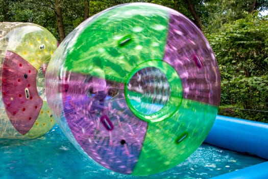 Water or aqua zorbing. Children play inside the inflatable transparent roller floating in swimming pool. Water walking or zorbing very popular fun activity and suitable for all ages.