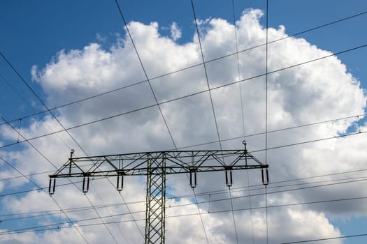 Power generation, transmission and distribution concept. Close-up of a electricity supply pylon and the high voltage power lines against a blue cloudy sky. Facilities for the transmission of electrical energy.