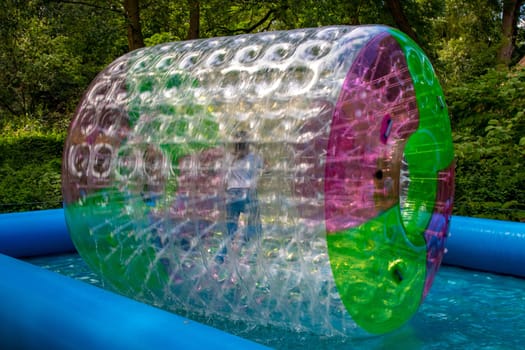 Water or aqua zorbing. Children play inside the inflatable transparent roller floating in swimming pool. Water walking or zorbing very popular fun activity and suitable for all ages.