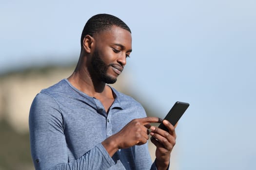 Man with black skin using smart phone in the mountain a sunny day