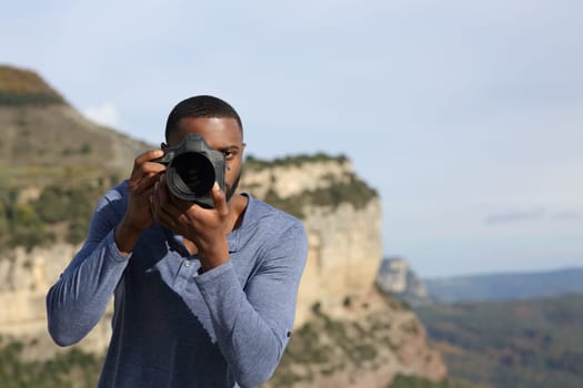 Front view portrait of a man with black skin taking photos with camera dslr in the mountain