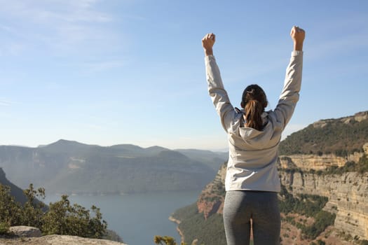 Back view portrait of a happy trekker raising arms in nature celebrating success