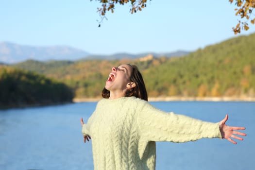 Excited woman screaming to the air outstretching arms in a lake in winter