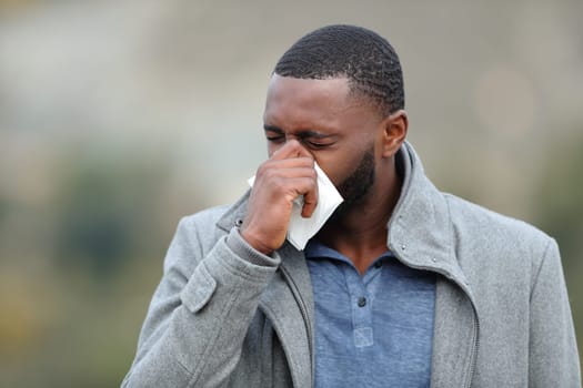 Sick guy with black skin blowing on tissue outdoors in winter