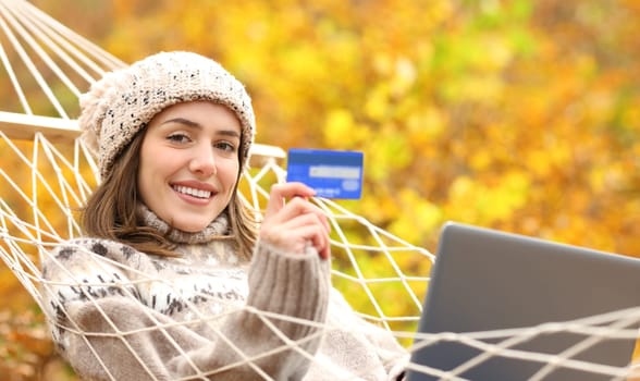 Happy woman on hammock showing credit card on winter holiday