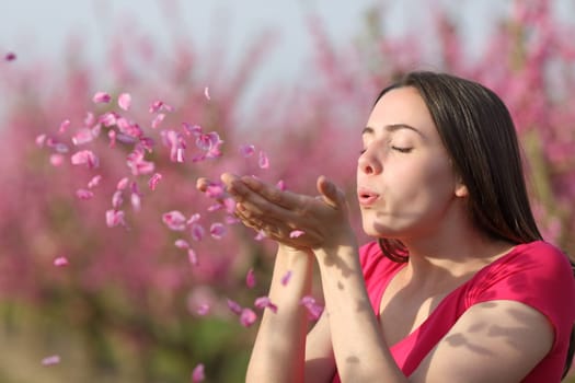 Woman blowing flower petals to the air from hands in a pink field