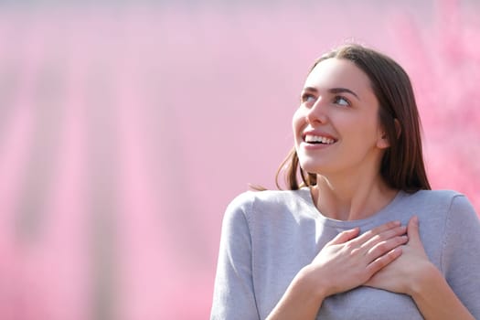 Happy woman smiling with hands on heart looking at side in a beautiful blurred pink field