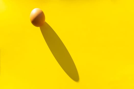 Brown organic raw egg on a yellow background with a hard shadow.