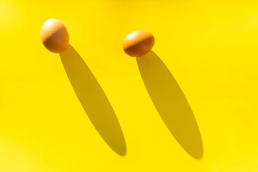 Two brown farm eggs on a yellow background in bright light, a concept of minimalism.