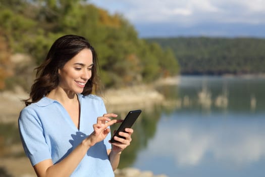 Happy woman checking smart phone in nature
