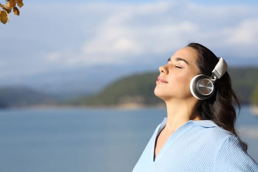Side view portrait of a relaxed woman wearing headphones meditating in a lake