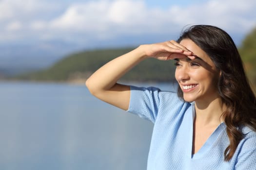 Happy woman looking away protecting from sun with hand in a lake