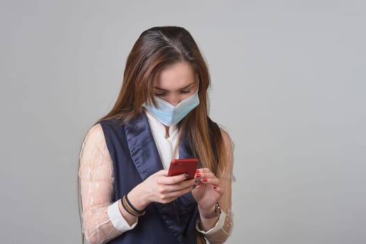 A girl in a medical mask with a phone in her hands. High quality photo