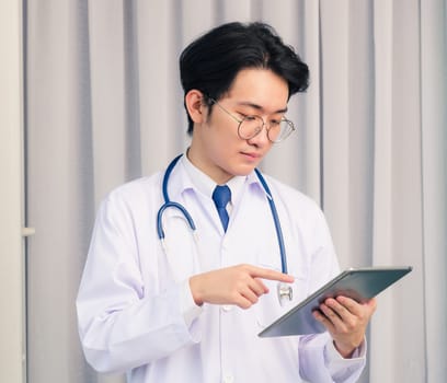 Portrait closeup of Happy Asian young doctor handsome man smiling in uniform and stethoscope neck strap holding and point smart digital tablet and looking to the tablet, healthcare medicine concept