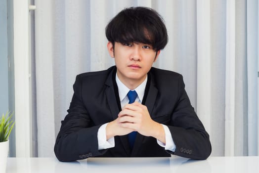 Work from home, Close up face of Asian young businessman video conference call or facetime he looking to camera sitting and holding hands to listen to colleagues explain the work on desk at office