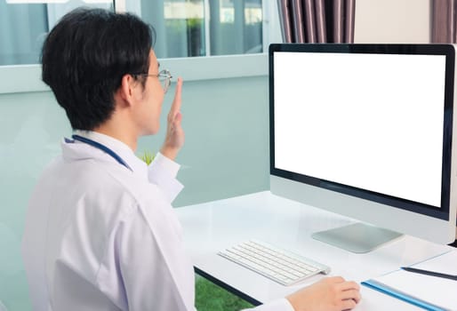 Asian young handsome doctor man wearing a doctor's dress and stethoscope video conference call or facetime raise hand say hello to patient he smiling on desk at hospital office, Health medical care