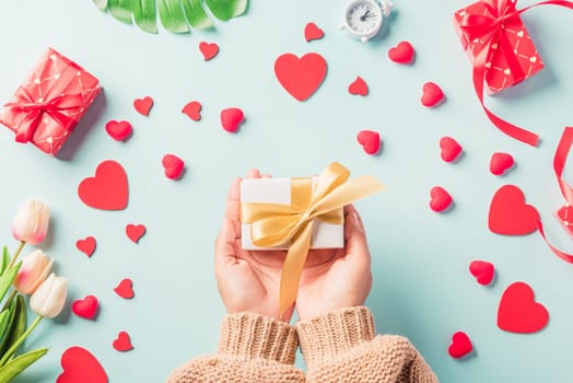 Valentine's day and birthday. Woman hands holding gift or present box decorated and red heart surprise on blue background, Female's hand hold gift box package in craft paper Top view flat lay